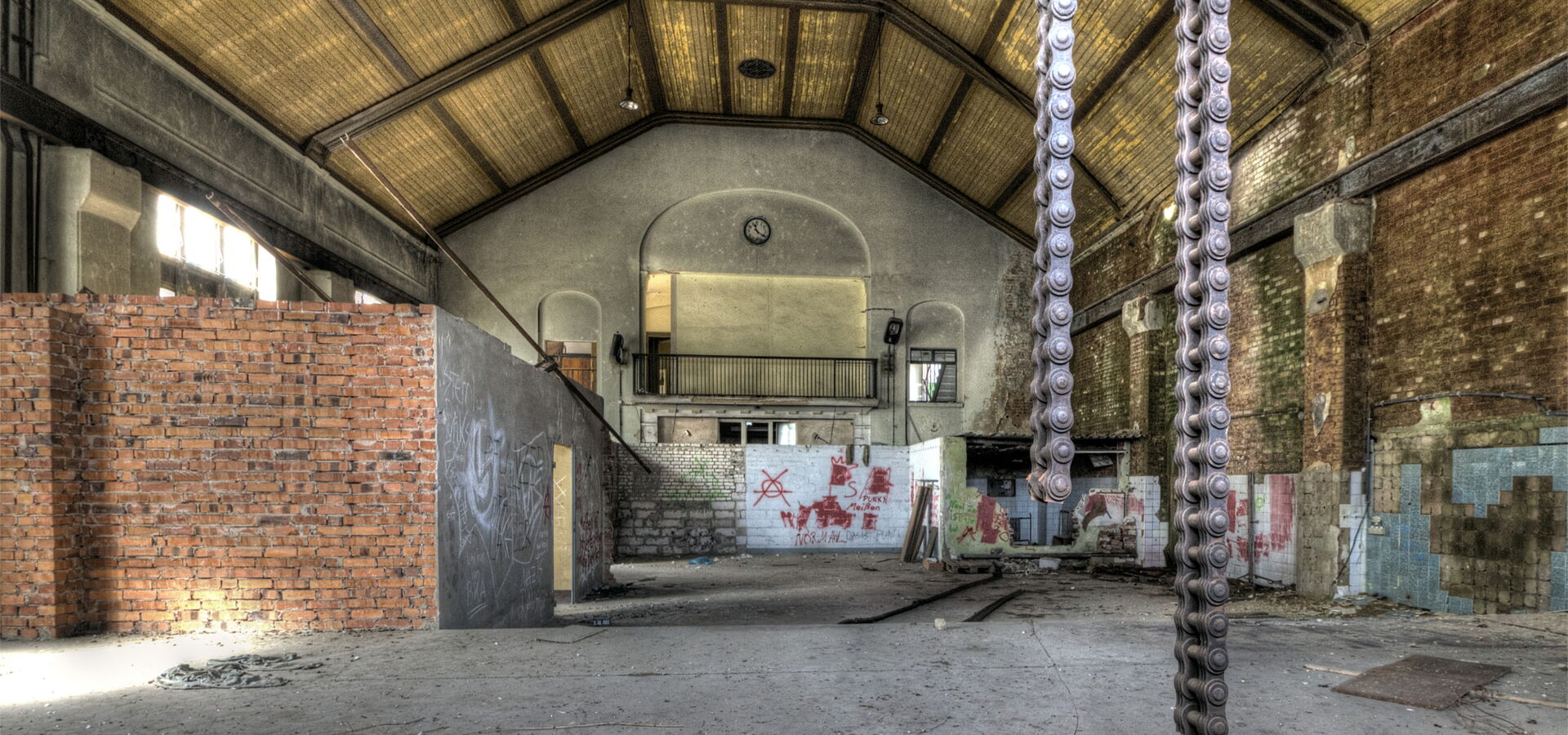 Geräumige Industriehalle mit Ketten und Graffiti.